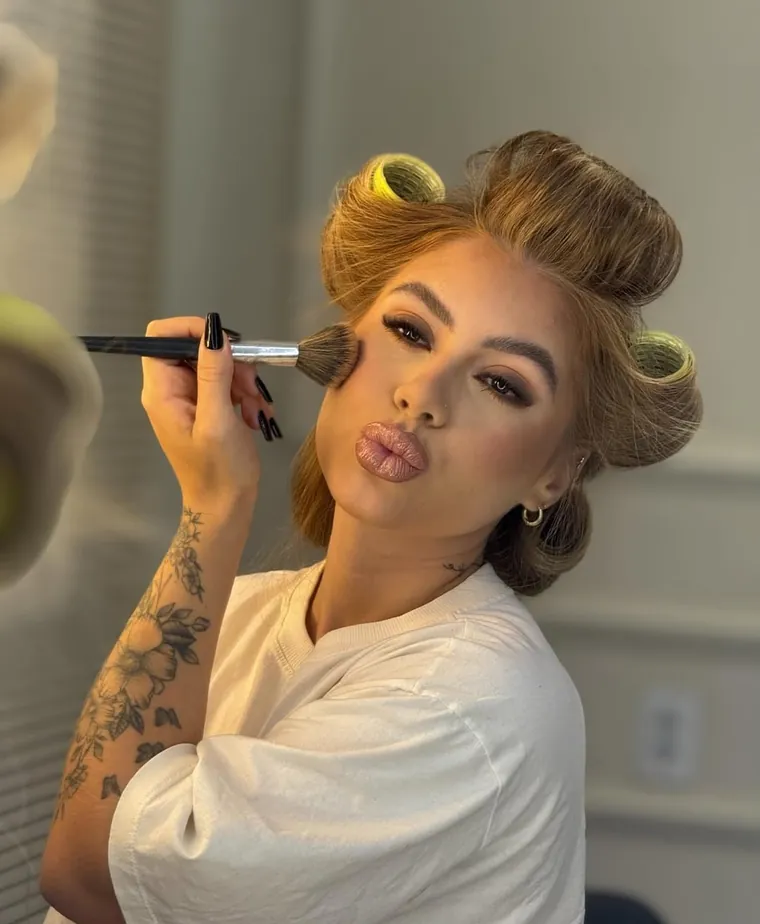 Bell se maquiando, com bobes no cabelo