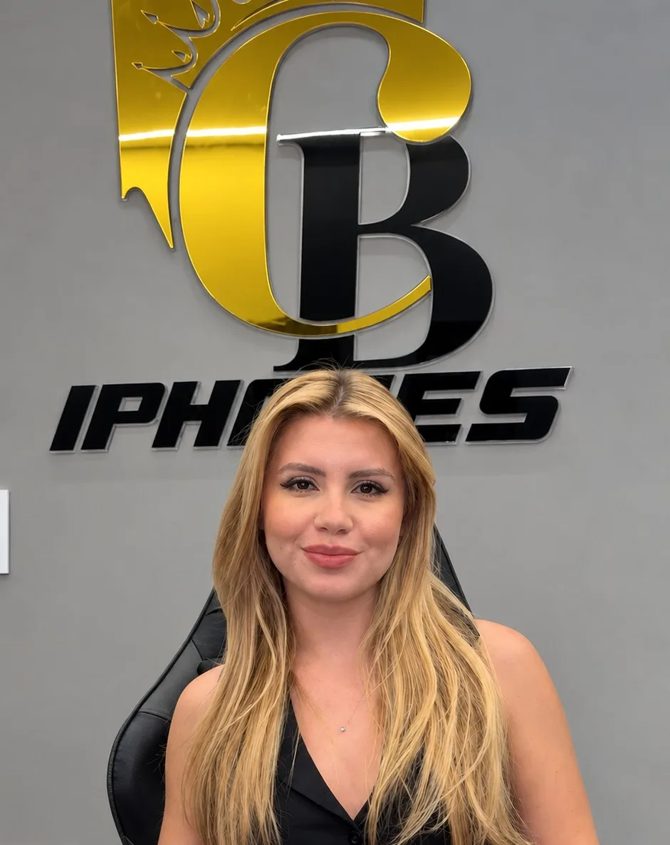 Bell sorrindo diante do letreiro dourado e preto da CB iPhones